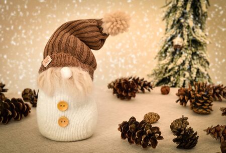 Decorated handmade gnome with pine cones on the table in front of the Christmas tree and snowy backgroundの写真素材