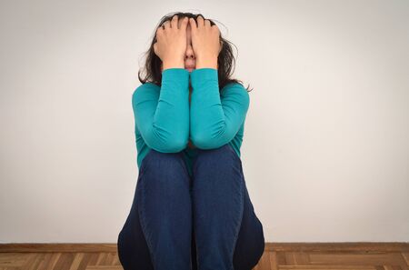 Depressed and sad woman covering her face with hands and sitting on the floor in the empty roomの写真素材