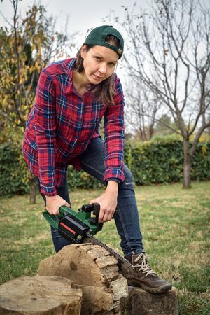 Female lumberjack holding chainsaw on the log and looking at the cameraの写真素材