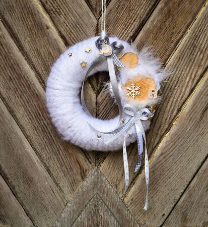 Decorated handmade Christmas wreath hanging on the rope on the rustic wooden doorの写真素材