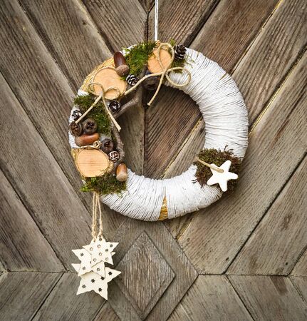 Decorated handmade Christmas wreath hanging on the rope on the rustic wooden doorの写真素材