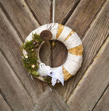 Decorated handmade Christmas wreath hanging on the rope on the rustic wooden doorの写真素材