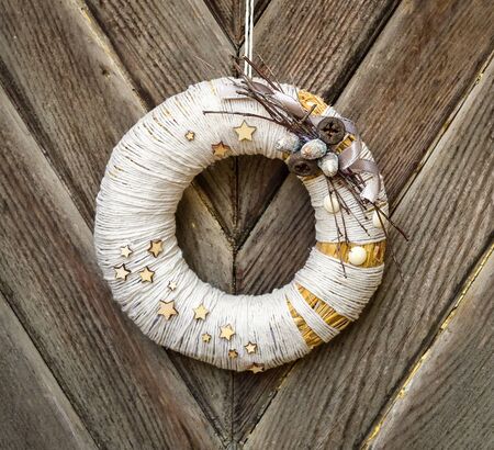 Decorated handmade Christmas wreath hanging on the rope on the rustic wooden doorの写真素材