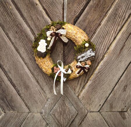 Decorated handmade Christmas wreath hanging on the rope on the rustic wooden doorの写真素材