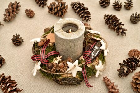 Decorated handmade Christmas wreath with candle and pine cones on the tableの写真素材