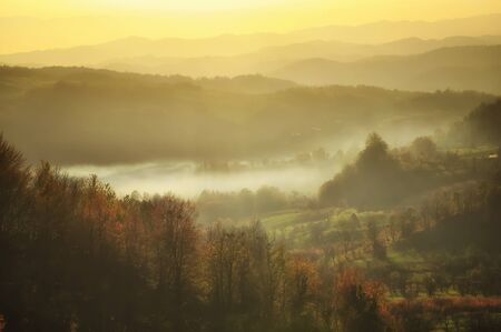 Beautiful autumn mountain in the sunset mist. Glowing sunset on the autumn forest. Lens flare effect. Soft focus.の写真素材