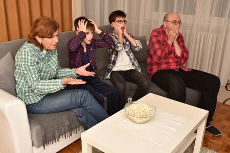 Family sitting on the sofa in the living room, watching a sports match on TV and cheering. They are very upset after their favorite team receiving a goal.の写真素材