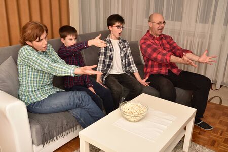 Family sitting on the sofa in the living room, watching a sports match on TV and cheering. They are very upset after their favorite team receiving a goal.の写真素材