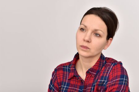 Portrait of a thoughtful woman with hair bun and tartan shirt. Copy space on the left side.の写真素材