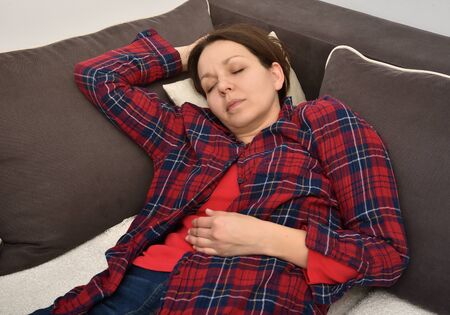 Beautiful tired woman wearing plaid shirt napping or sleeping on the sofa in the living room at homeの写真素材