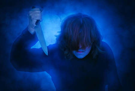Frightening woman with hair covering her face holding a knife. Smoke effect applied. Halloween and horror concept.の写真素材