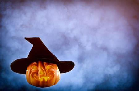 Halloween pumpkin with a black hat on the smokey background with copy space. Halloween and horror concept.の写真素材