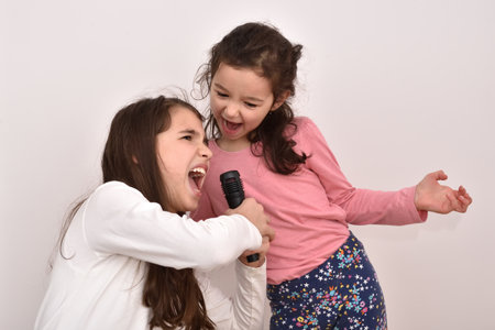 Two happy sisters fooling around and singing a song on a microphone. Emotional portrait of happy children.の写真素材