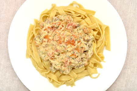 Close-up of Italian traditional tagliatelle pasta with creamy sauce, pork pieces, carrot slices and chopped parsley on the white plate. Top view.の写真素材