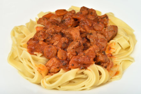 Close-up of Italian traditional tagliatelle pasta with tomato sauce, pork pieces, carrot slices, onion pieces and chopped parsley on the white plate. Selective focus.の写真素材
