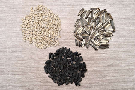 Three separate piles of sunflower seeds (peeled, black, striped black and white) on the rustic wooden table. Top view.の写真素材