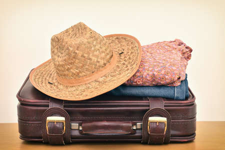 Vintage leather suitcase with straw hat, floral shirt and jeans on the brown wooden table. Copy space. Travel baggage concept.の写真素材
