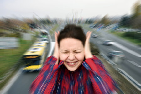 Woman with closed eyes covering her ears in the street while vehicles are passing by fast in the background. Noise pollution concept. Radial blur filter applied.の写真素材