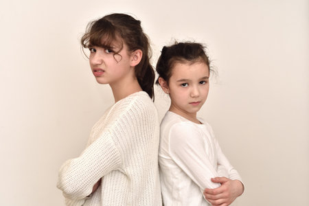Two angry and frowning sisters standing back to back, not talking to each otherの写真素材