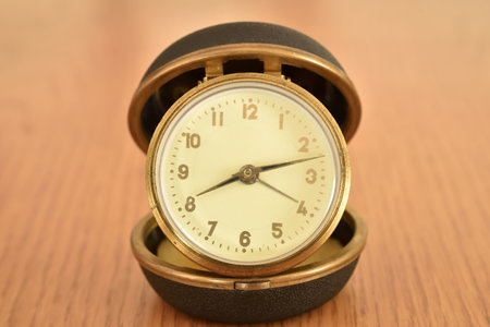 Old small clock on the brown wooden table. Close-up. Retro style photo.の写真素材