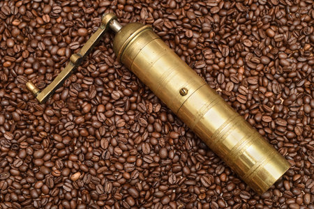 Old golden manual coffee grinder lying down on the heap of fresh roasted coffee beansの写真素材