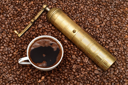Cup of coffee, old golden manual coffee grinder and heap of fresh roasted coffee beans on the tableの写真素材