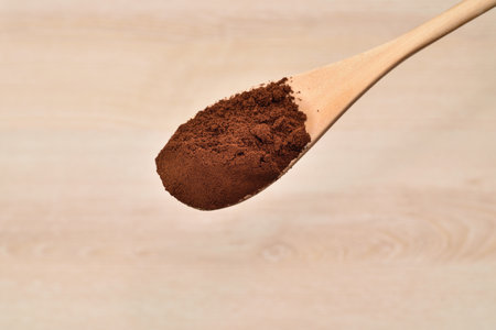 Coffee powder in the wooden spoon above the light brown wooden table. Close-up. Top view.の写真素材