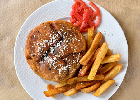 Traditional Kefalonian meat pie with French fries and two tomato slices served on the white plate. Top view.の写真素材