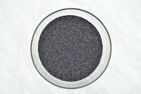 Poppy seeds in the glass bowl on the light gray marble table texture. Top view.の写真素材