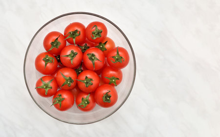 Cherry tomatoes in the glass bowl on the light gray marble table texture. Copy space. Top view.の写真素材