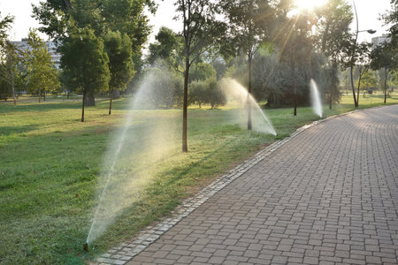 Automatic sprinkler system watering the lawn in the summer morning. Irrigation in the city park. Flying splashes of water falling on the grass. Rotating fountain.の写真素材
