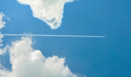 Airplane leaving white contrail in the blue sky with white clouds. Copy space.