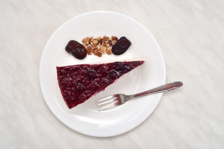 Piece of homemade cheesecake, broken walnut kernels, fresh dates and small dessert fork on the white plate. Top view.の写真素材
