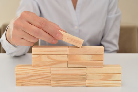 Hand of a businesswoman putting or removing wooden block on the top of wooden blocks stacked in the...
