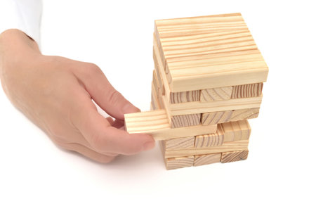 Hand of a businesswoman removing wooden block on the wooden tower on the white background. Concept of risk and bad strategy in business.の写真素材