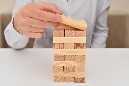 Hand of a businesswoman putting or removing wooden block on the top of wooden tower on the table. Concept of strategy and solution in business.の写真素材