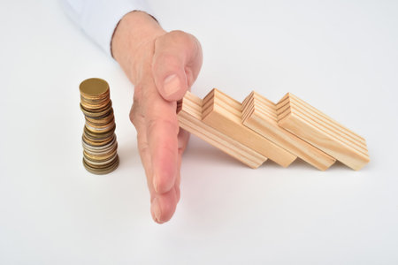 Hand of a businesswoman stopping falling wooden blocks on stacked coins. Selective focus. Concept of strategy and risk in business.の写真素材