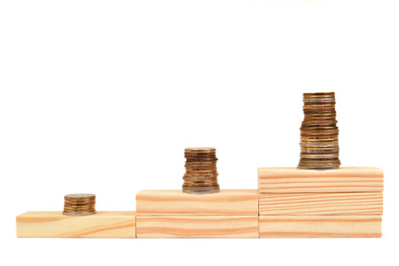 Stacks of coins on the wooden blocks stacked in the shape of stairs on the white background. Copy space. Business and financial growth concept.の写真素材