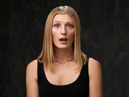 Woman surprised. Model with blonde hair in a black shirt on a dark background.の写真素材
