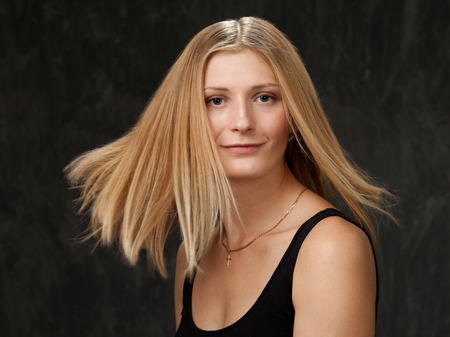 Portrait of a smiling young blonde woman with flowing hair on a dark backgroundの写真素材