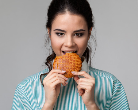 Frontal  portrait of an attractive brunette biting a cookie, looking down, grey backgroundの写真素材