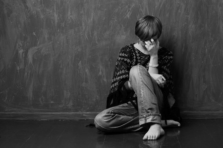 Barefoot girl crying on the floor near the wall. Black and white image.の写真素材