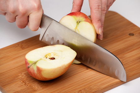woman's hand with a kitchen knife cut a large red apple in half on a wooden boardの写真素材