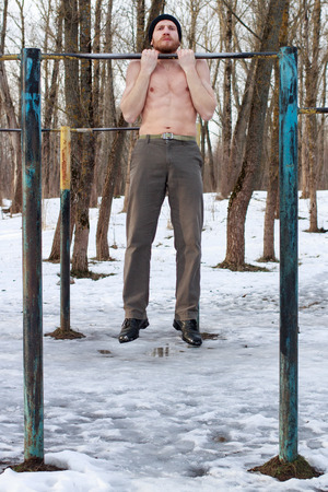 A young bearded man in a black hat with naked torso doing street workout. Fitness model doing...