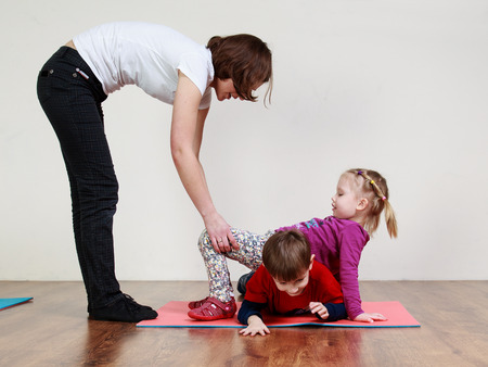 Physiotherapy for children. A little boy anf a girl are doing an exercise at the gym with the help of trainerの写真素材