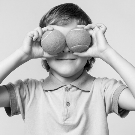 Children. Little boy holding tennis balls instead of the eyes, smiling, black and whiteの写真素材
