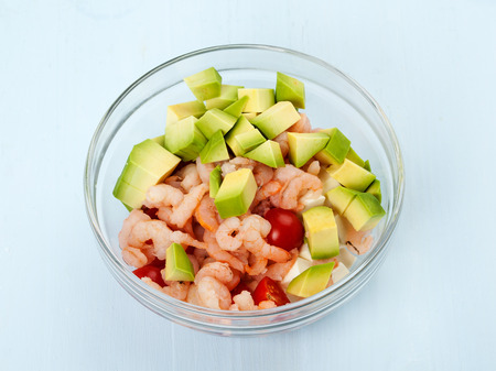 Food. Preparing a salad. A plate with shrimps, avocado and other ingredients on blue backgroundの写真素材