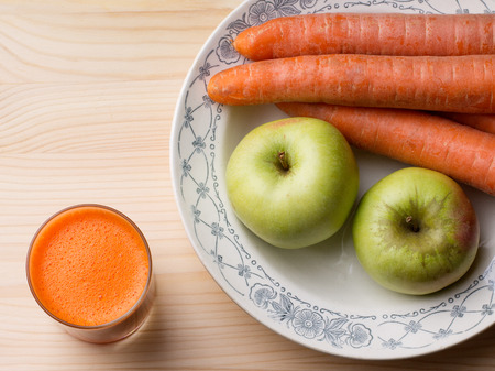 Food. Fruits and vegetables. Two apples, some carrots  on a plate, a glass of fresh juice on wooden backgroundの写真素材