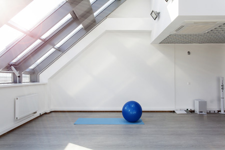 Gym for fitness exercises. Fitbol and mat  lie on the floor. The room is flooded with sunlight from the window, the glare on the white wall. Audio system with speakers in the background.の写真素材