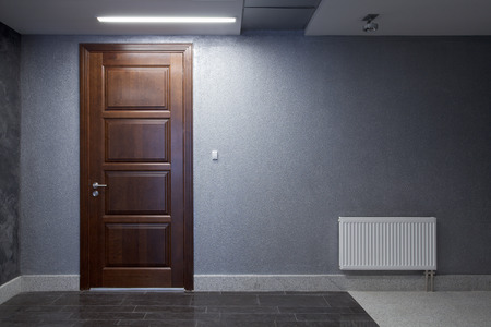 Interior. Office. A gray wall with a brown wooden door and a radiatorの写真素材